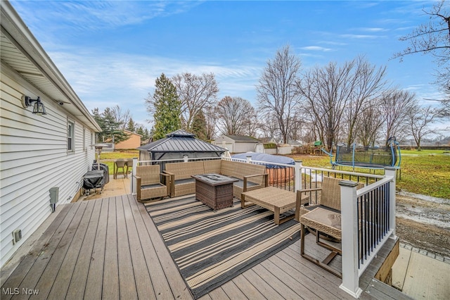 wooden terrace featuring a trampoline, an outdoor living space, and a gazebo