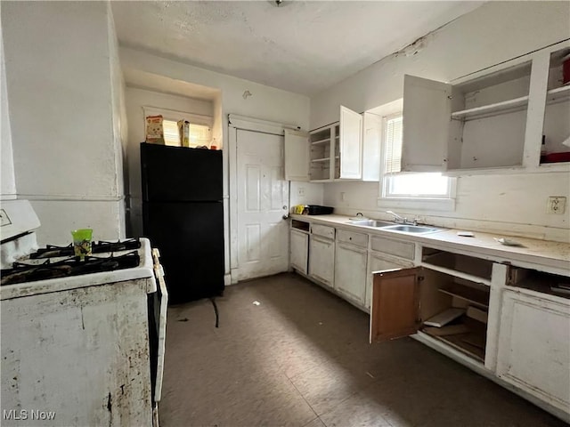 kitchen featuring white gas range, sink, black fridge, and white cabinets