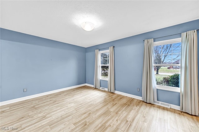 empty room with a textured ceiling and light hardwood / wood-style floors