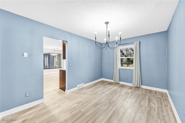 unfurnished dining area with an inviting chandelier, light hardwood / wood-style floors, and a textured ceiling