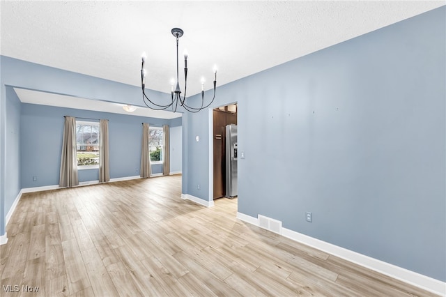 unfurnished dining area featuring a notable chandelier, a textured ceiling, and light hardwood / wood-style flooring