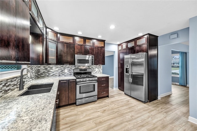 kitchen featuring appliances with stainless steel finishes, tasteful backsplash, sink, light stone counters, and light wood-type flooring