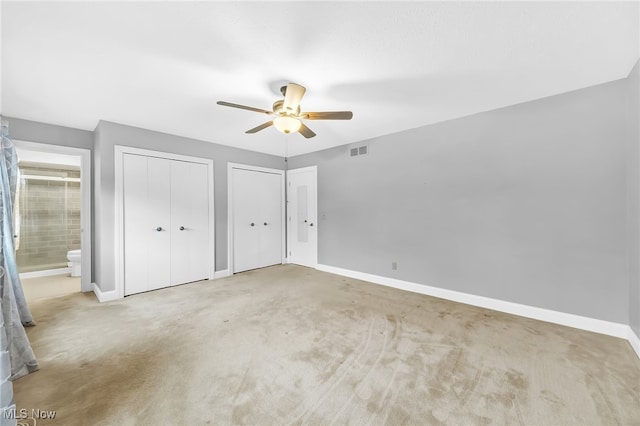 unfurnished bedroom with multiple closets, ceiling fan, light colored carpet, and ensuite bath