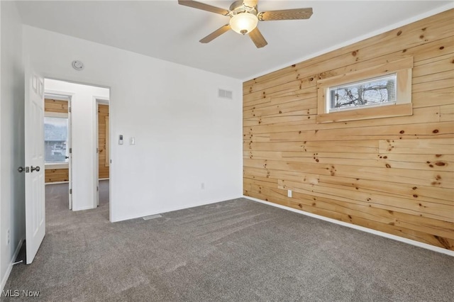 unfurnished room featuring wooden walls, ceiling fan, and carpet flooring