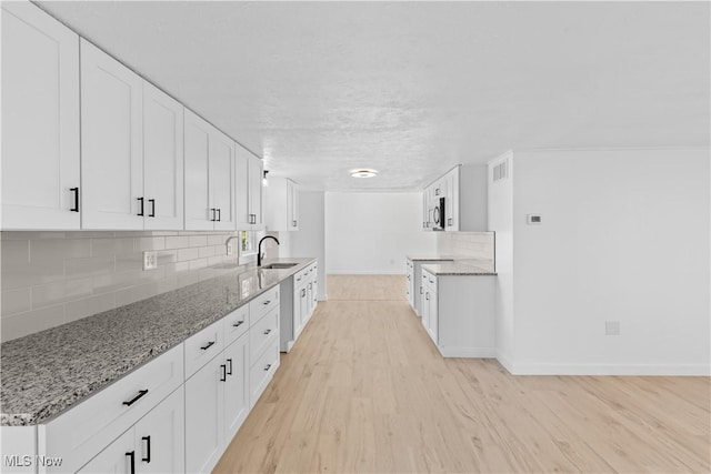 kitchen featuring tasteful backsplash, white cabinetry, sink, light stone counters, and light hardwood / wood-style floors