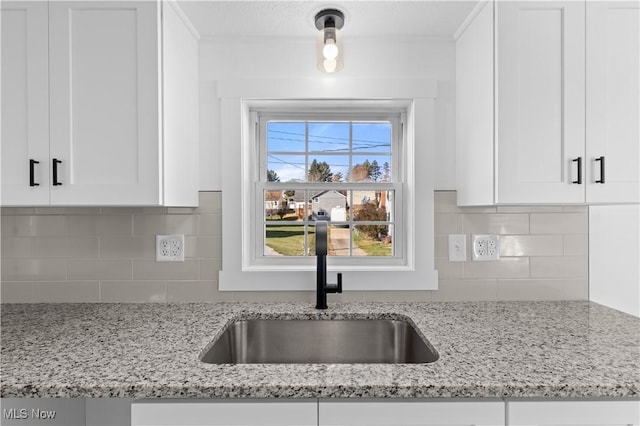 kitchen with white cabinetry, light stone countertops, and sink