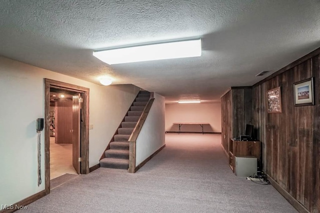 basement featuring light carpet, a textured ceiling, and wood walls