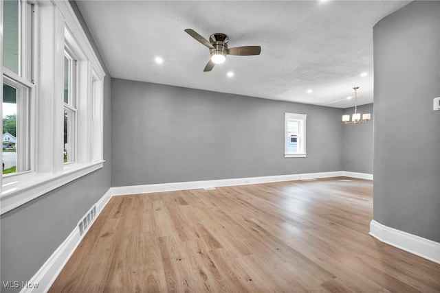 empty room featuring ceiling fan with notable chandelier, a wealth of natural light, and light hardwood / wood-style floors