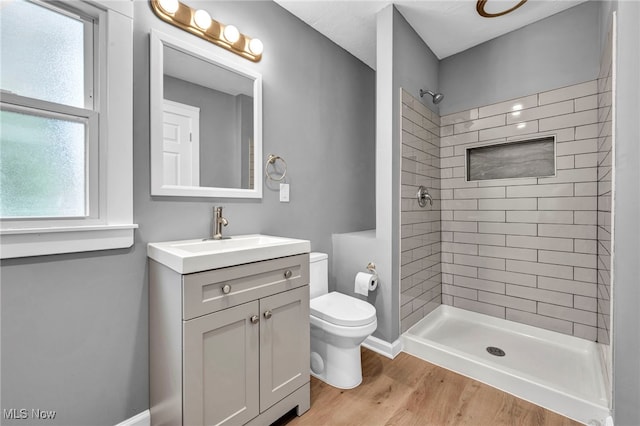 bathroom featuring hardwood / wood-style flooring, tiled shower, vanity, and toilet