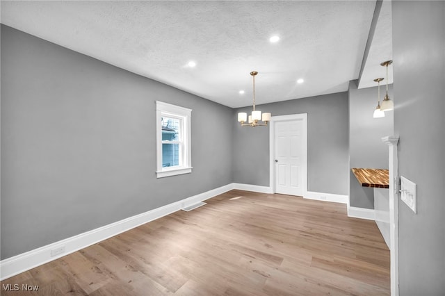 spare room with a textured ceiling, light hardwood / wood-style flooring, and a notable chandelier