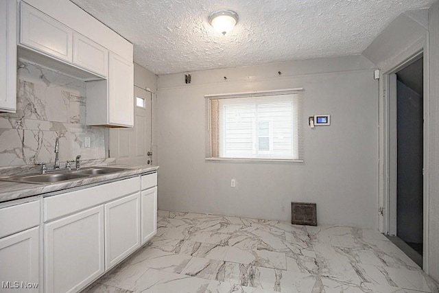 kitchen with white cabinetry, decorative backsplash, sink, and a textured ceiling