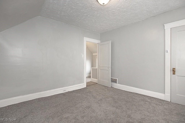 spare room featuring lofted ceiling, carpet floors, and a textured ceiling