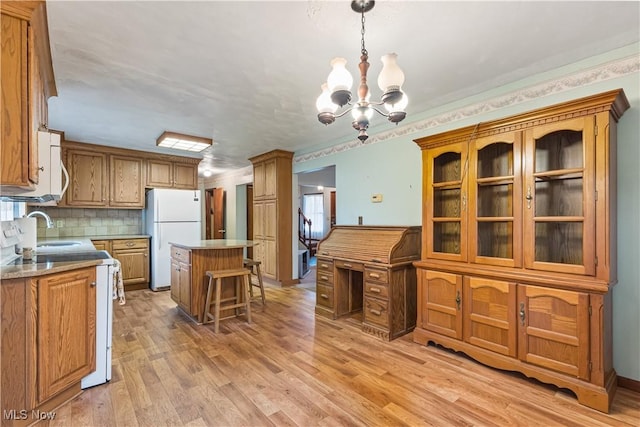 kitchen with sink, decorative light fixtures, a center island, light hardwood / wood-style flooring, and white appliances