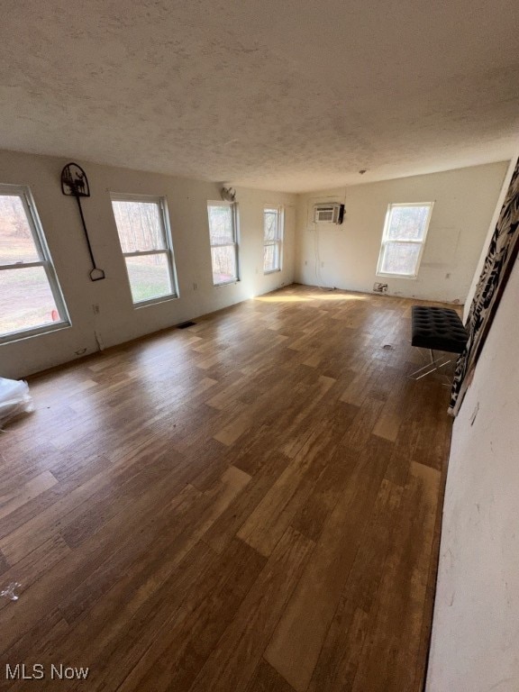 unfurnished living room featuring dark hardwood / wood-style floors, a wall mounted AC, and a textured ceiling