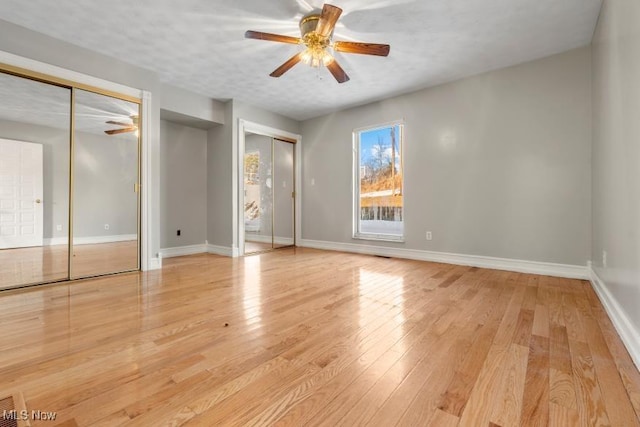 unfurnished bedroom featuring two closets, baseboards, a ceiling fan, and hardwood / wood-style floors