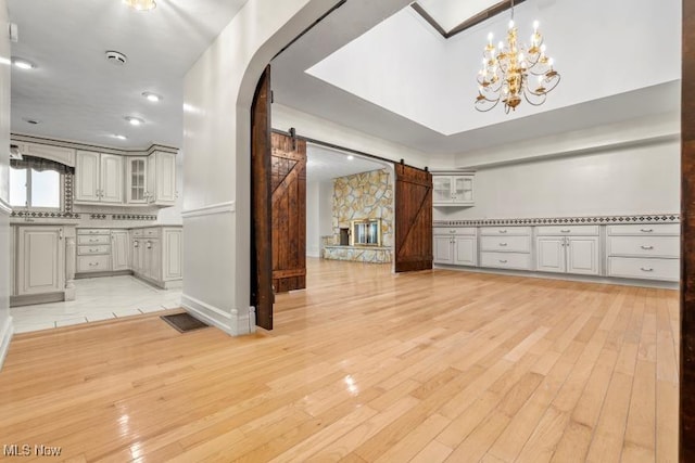 interior space with a barn door, arched walkways, light wood finished floors, and an inviting chandelier