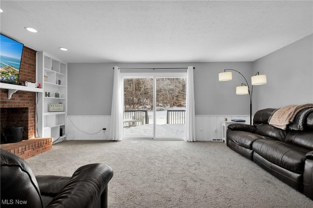 living room with a brick fireplace, built in shelves, carpet floors, and a textured ceiling