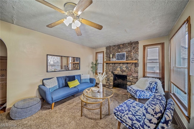 living room featuring ceiling fan, a fireplace, and a textured ceiling