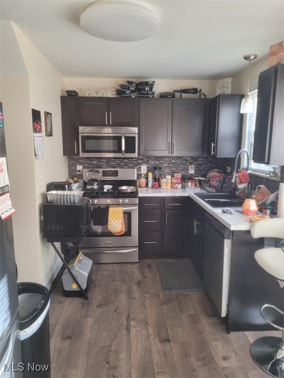 kitchen with sink, dark hardwood / wood-style floors, pendant lighting, stainless steel appliances, and backsplash