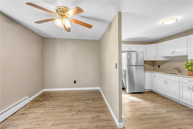 24512 Emery Rd, Warrensville Heights, OH 44128 - kitchen featuring white cabinetry, sink, stainless steel fridge, baseboard heating, and light wood-type flooring
