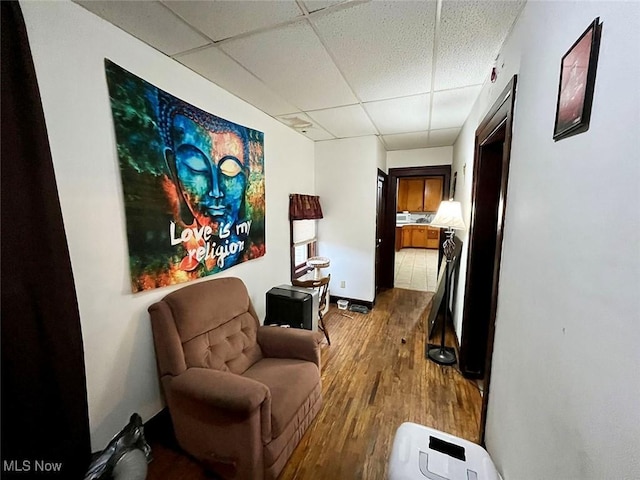 sitting room featuring wood-type flooring and a drop ceiling