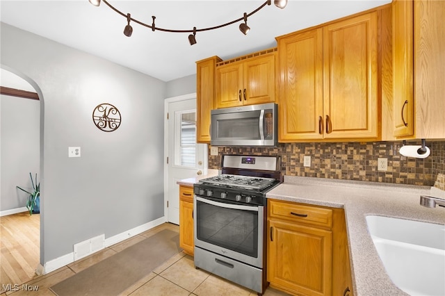 kitchen with appliances with stainless steel finishes, sink, light tile patterned floors, and decorative backsplash