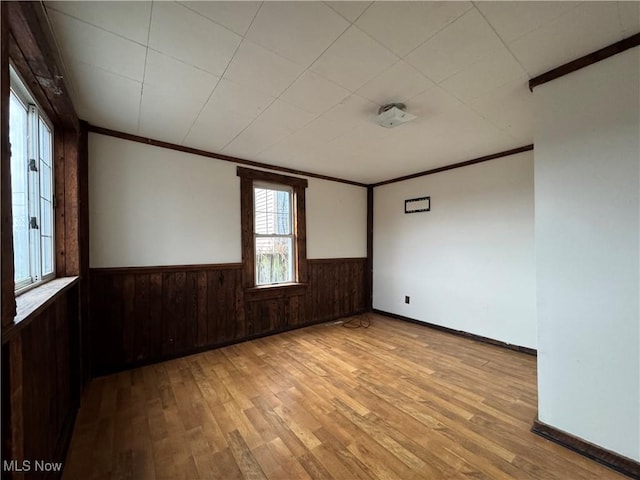 spare room featuring crown molding, wood walls, and light hardwood / wood-style flooring