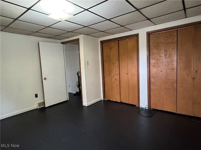 unfurnished bedroom featuring two closets and a drop ceiling