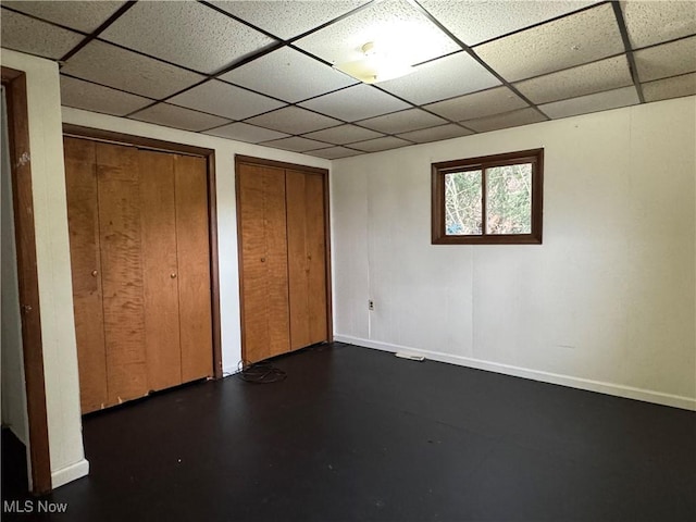 unfurnished bedroom featuring a drop ceiling and multiple closets