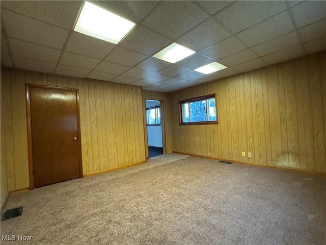 unfurnished room featuring a paneled ceiling, wooden walls, and carpet