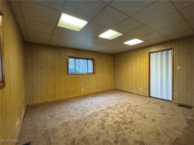 spare room with carpet flooring, a paneled ceiling, and wooden walls