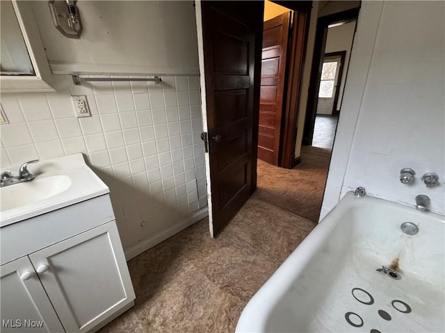 bathroom with vanity, tile walls, and a tub to relax in