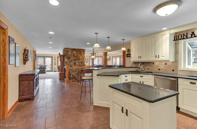 kitchen featuring sink, stainless steel dishwasher, kitchen peninsula, pendant lighting, and backsplash