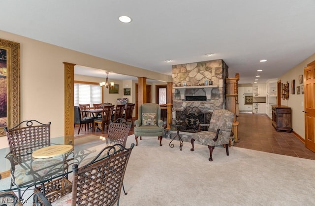 living room featuring an inviting chandelier, a stone fireplace, and carpet flooring