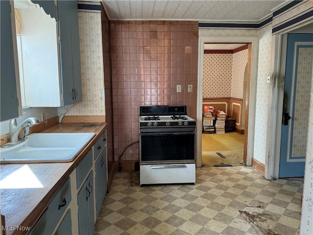 kitchen with gray cabinetry, sink, crown molding, and gas range oven