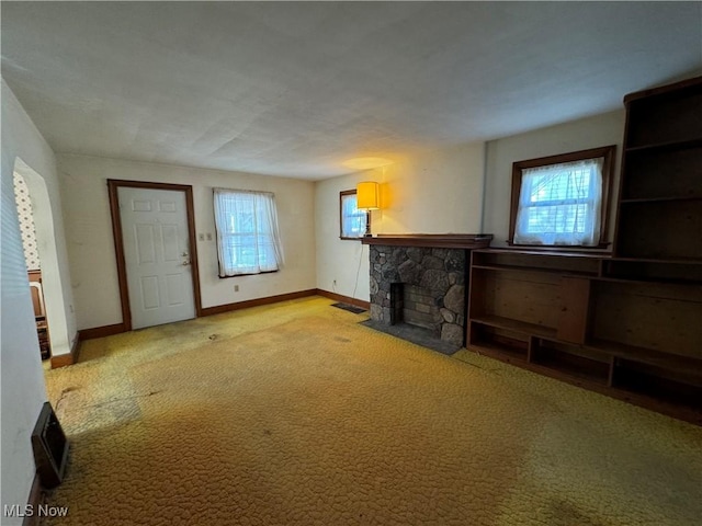 unfurnished living room with plenty of natural light, carpet flooring, and a stone fireplace