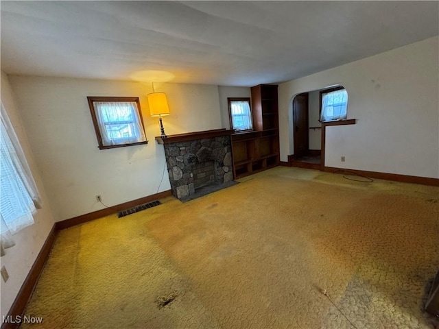 unfurnished living room featuring a stone fireplace, carpet floors, and a healthy amount of sunlight