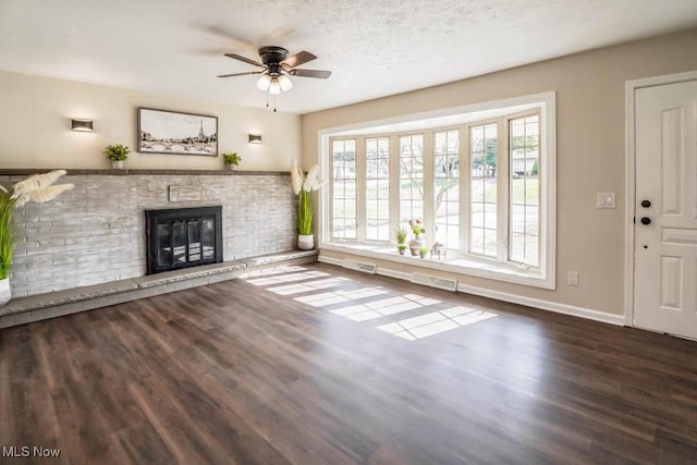 unfurnished living room with ceiling fan, dark hardwood / wood-style floors, a brick fireplace, and a textured ceiling