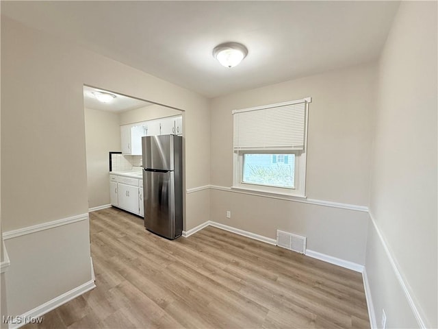 kitchen featuring tasteful backsplash, stainless steel fridge, white cabinets, and light wood-type flooring