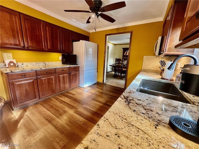 kitchen with sink, white fridge, light stone counters, light hardwood / wood-style floors, and crown molding