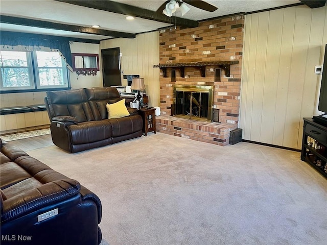 carpeted living room with ceiling fan, a fireplace, wooden walls, and beamed ceiling