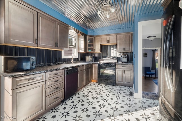 kitchen featuring a healthy amount of sunlight, sink, dark stone counters, and black appliances