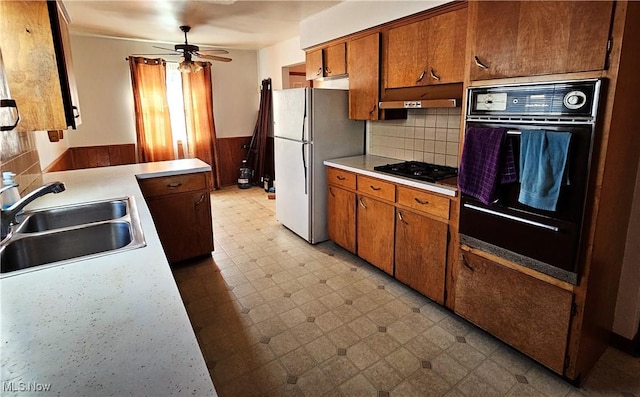 kitchen featuring sink, ceiling fan, wooden walls, black appliances, and decorative backsplash