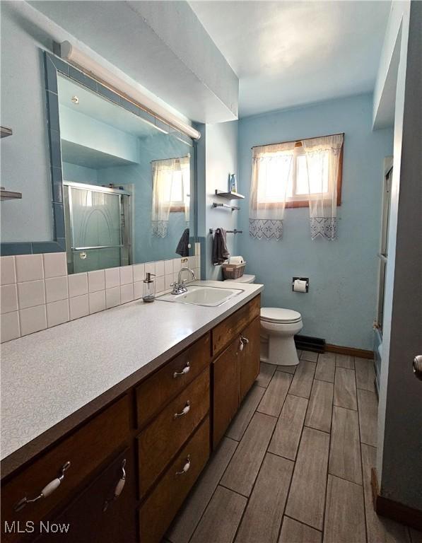 bathroom featuring tasteful backsplash, vanity, toilet, and a shower with shower door