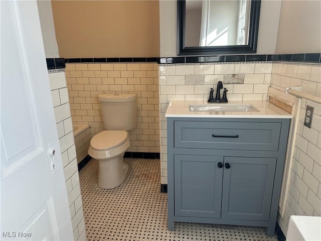 bathroom featuring toilet, a wainscoted wall, tile patterned flooring, vanity, and tile walls