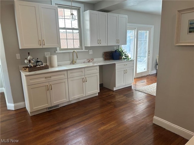 kitchen with dark wood-style floors, light countertops, visible vents, white cabinetry, and a sink