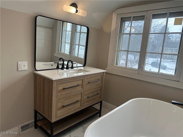 bathroom with lofted ceiling, visible vents, vanity, a freestanding tub, and baseboards