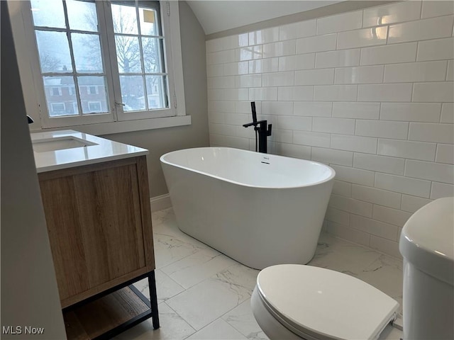 bathroom featuring marble finish floor, a soaking tub, vanity, and toilet