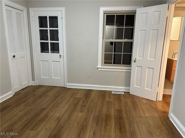 empty room featuring dark wood-type flooring, visible vents, and baseboards