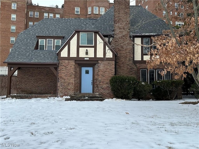 tudor house with stucco siding, a shingled roof, and brick siding